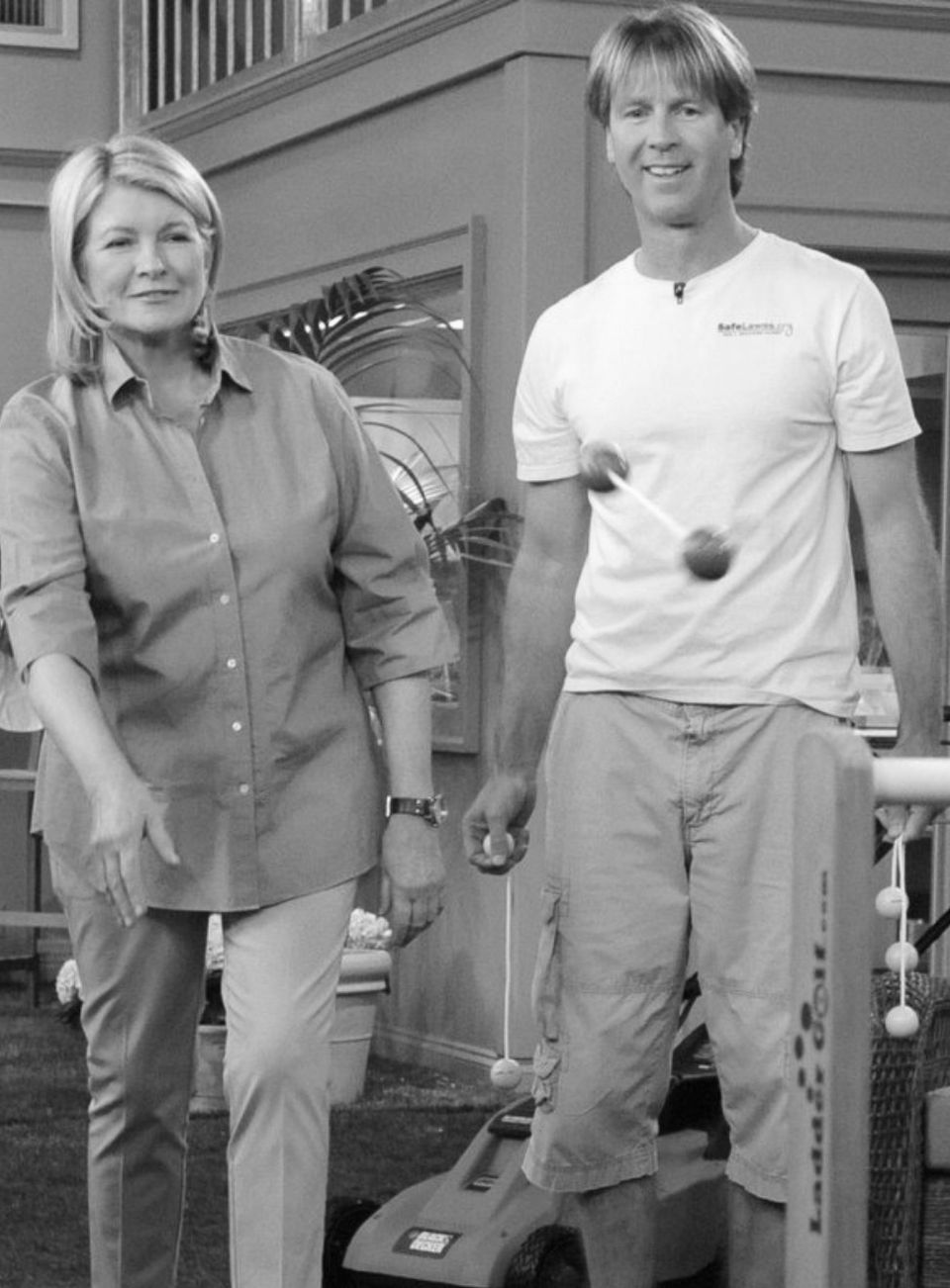 Paul Tukey in a SafeLawns T-shirt, standing beside a woman on a television set with a lawn mower behind them