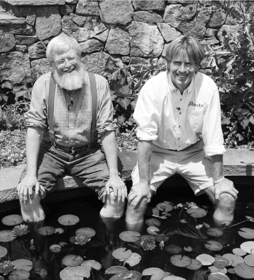Paul Tukey, right, and a bearded man sitting on the edge of a lily pond with their feet in the water